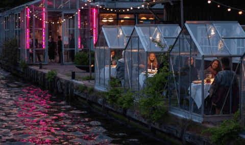 people dining in small glass structures by a river
