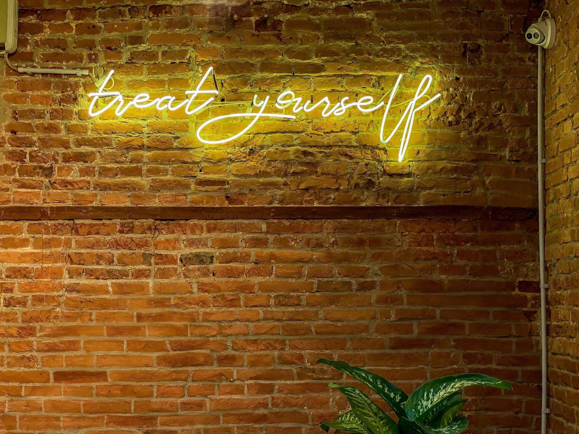 brick wall with neon sign that says "treat yourself"