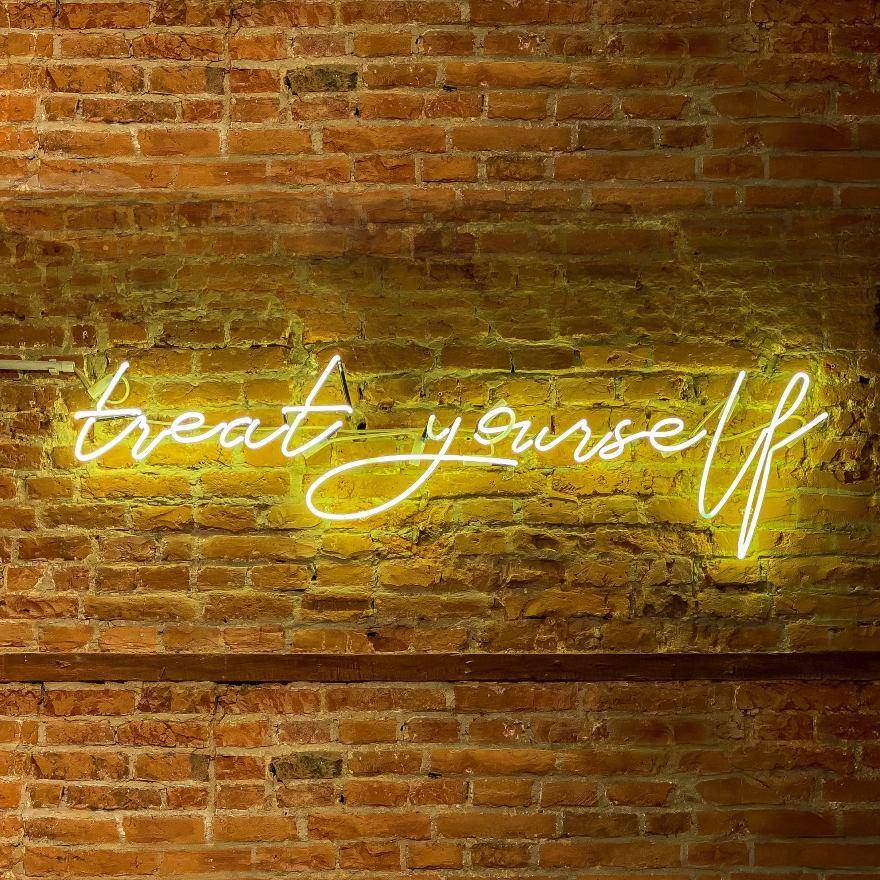 brick wall with neon sign saying "treat yourself"