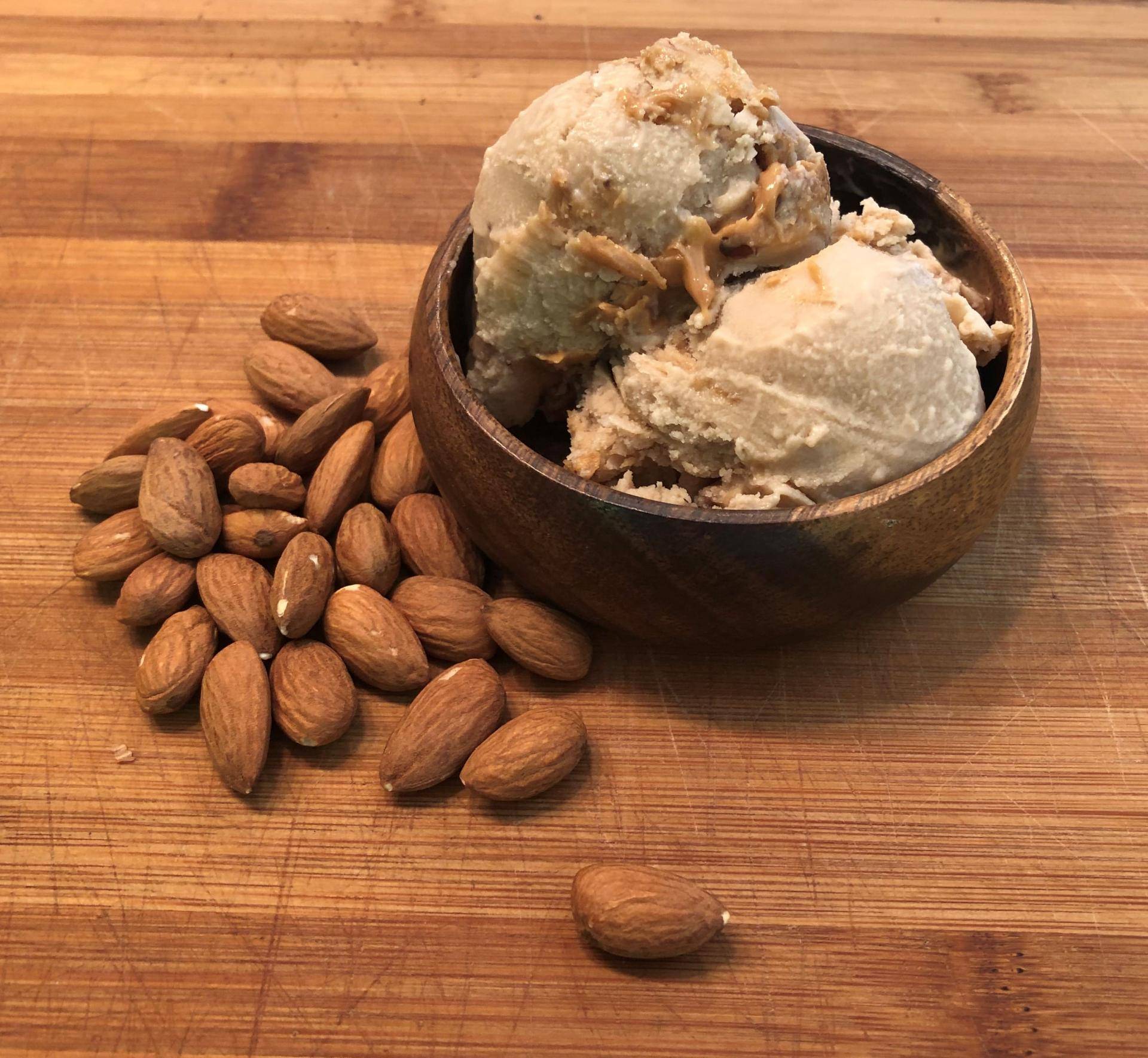 bowl of almond butter crunch ice cream with almonds on table next to it