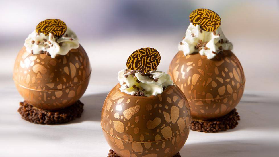 Dessert shells filled with iced coffee and whipped cream, with a chocolate plaque on top