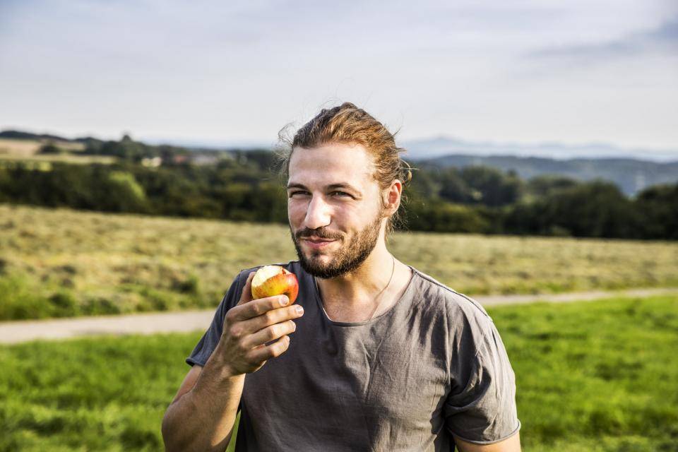 man eating apple in a field