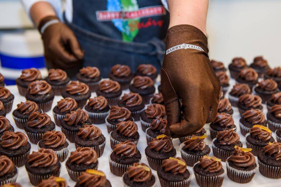A Barry Callebaut chef placing a piece of candied orange peel on a chocolate cupcake made with Bensdorp Natural Dark cocoa powder.