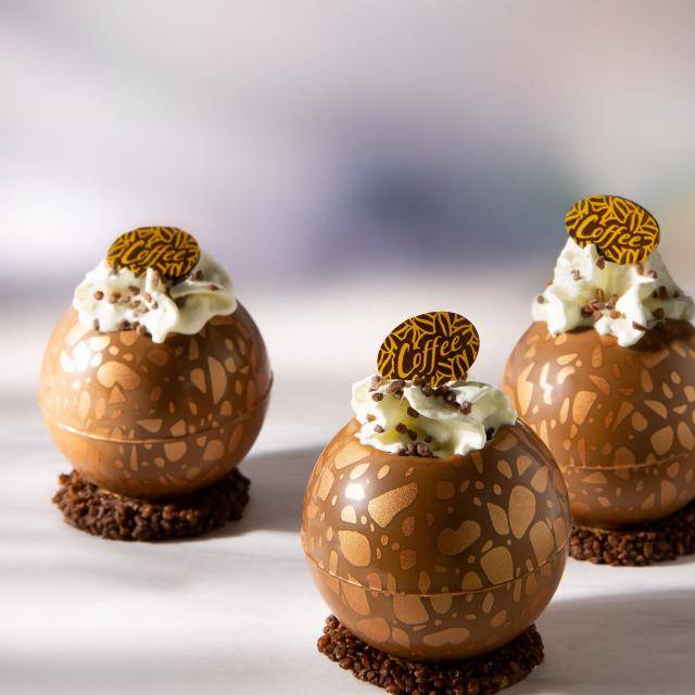 Dessert shells filled with iced coffee and whipped cream, with a chocolate plaque on top